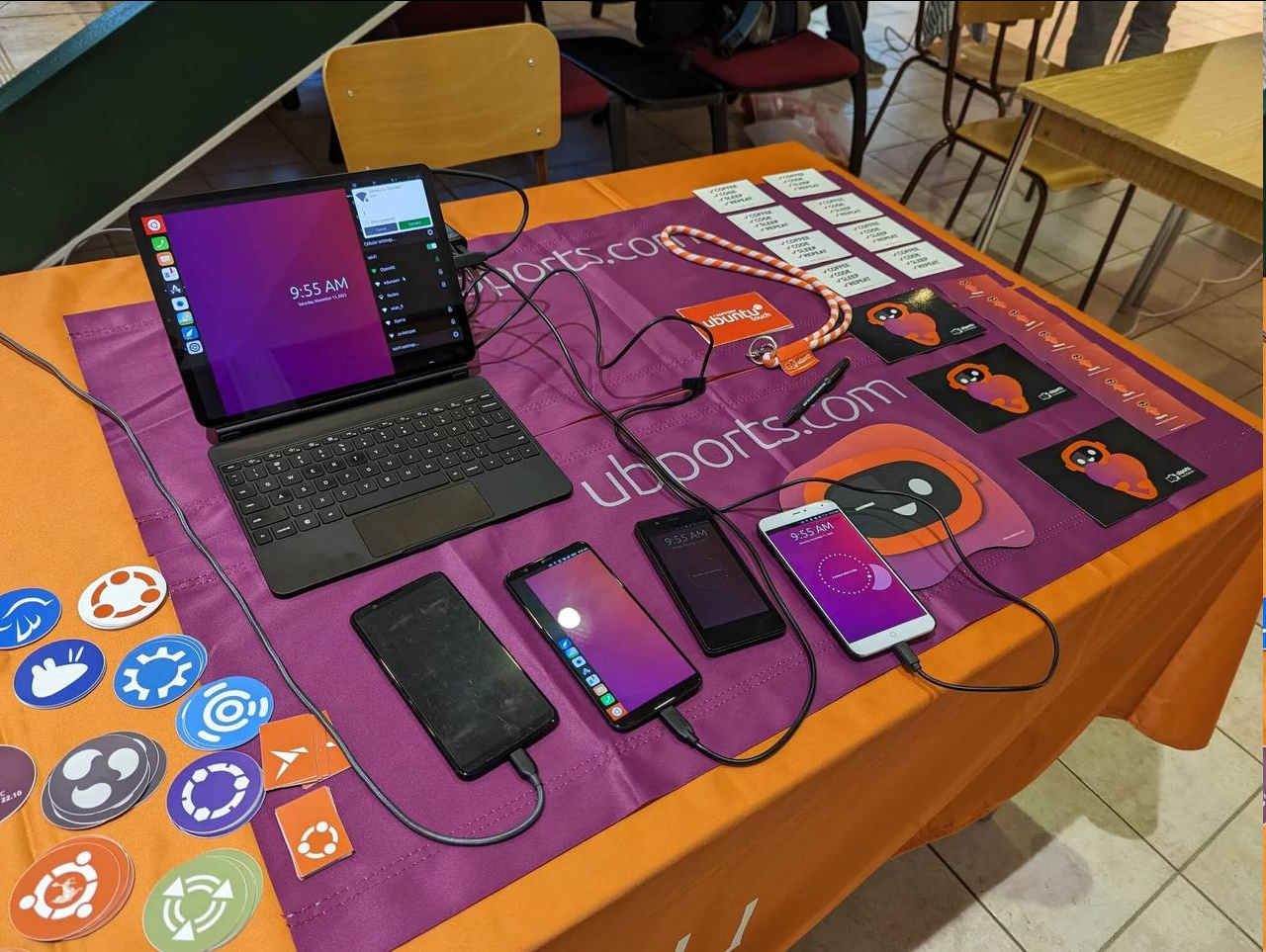 A bunch of different smartphones and a tablet running Ubuntu Touch, surrounded by stickers and UT merch.
